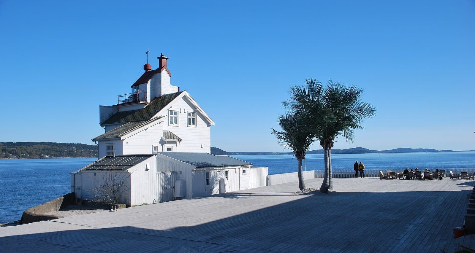 Filtvet fyr med palmene og stranden ved Villa Malla i forgrunnen, Oslofjorden bak (foto: Helge Høifødt, CC BY-SA 3.0, Wikimedia Commons)