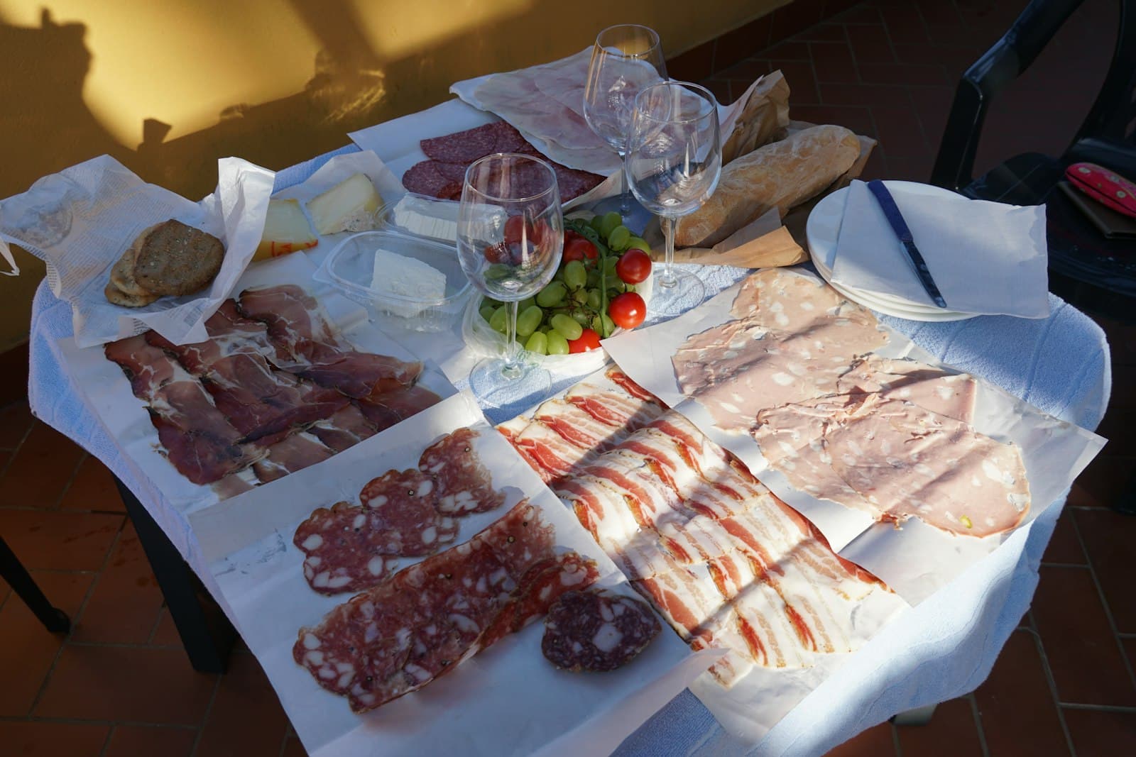 Italienske delikatesser på langbord i kveldssol — spekemat, oster og vin