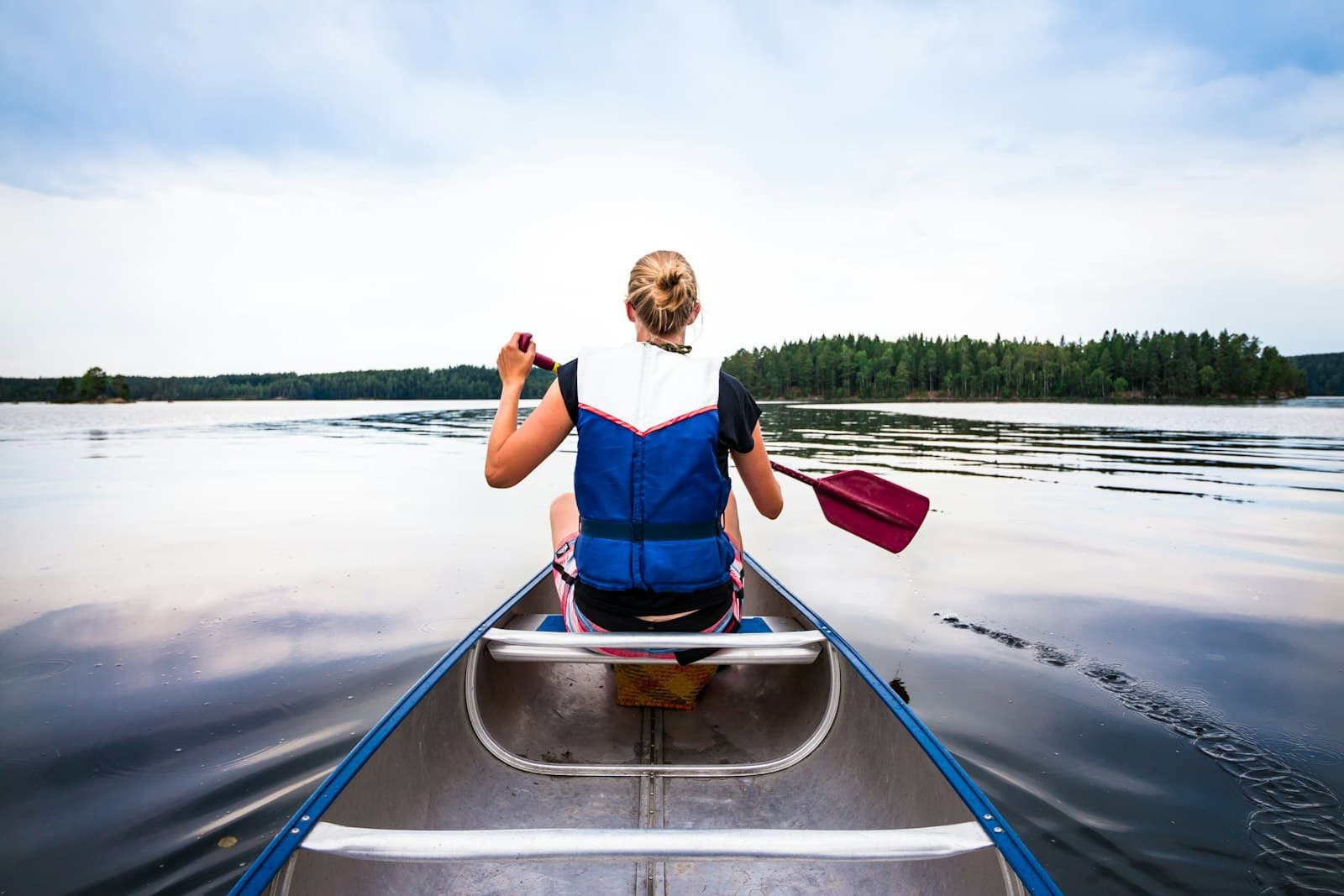 Padler i kano på et stille skogsvann med furukledde øyer (foto: Unsplash, fri kommersiell bruk)